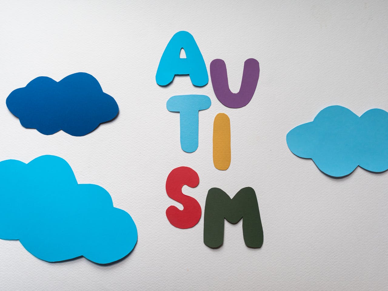 creative Vibrant letters spelling 'AUTISM' surrounded by blue paper clouds on a white background.